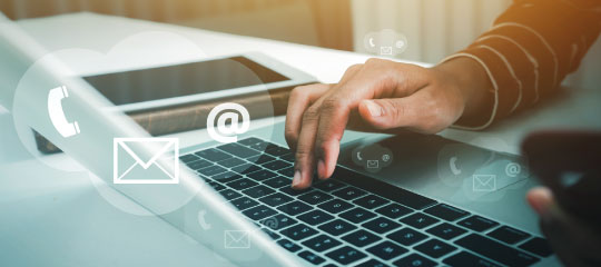 A hand is typing on the laptop and there is icon of call, email, and at the rate on the image